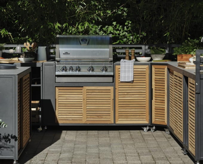 Zestaw kuchenny Fornax na świeżym powietrzu z nowoczesnym grillem i drewnianymi szafkami, otoczony bujną zielenią w otoczeniu przydomowego ogrodu.
