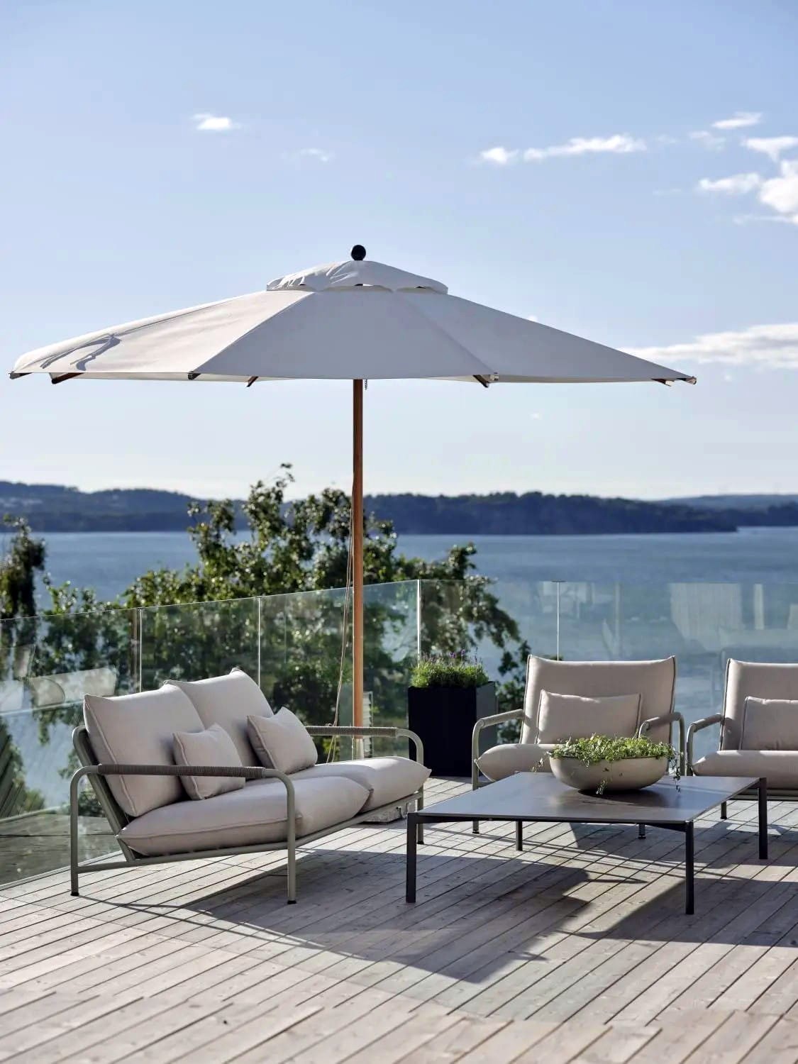 Na patio na świeżym powietrzu z widokiem na jezioro i odległe góry znajduje się duży biały parasol, dwa wyściełane fotele i stolik kawowy z ozdobną rośliną. Część wypoczynkowa znajduje się na drewnianym tarasie ze szklanymi balustradami.