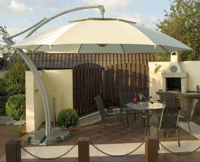 Duży, szary parasol zewnętrzny z zakrzywionym metalowym stojakiem. Parasol ma konstrukcję wspornikową i solidną podstawę. Tkanina parasola jest naciągnięta na szeroką ramę, zapewniając duży cień.